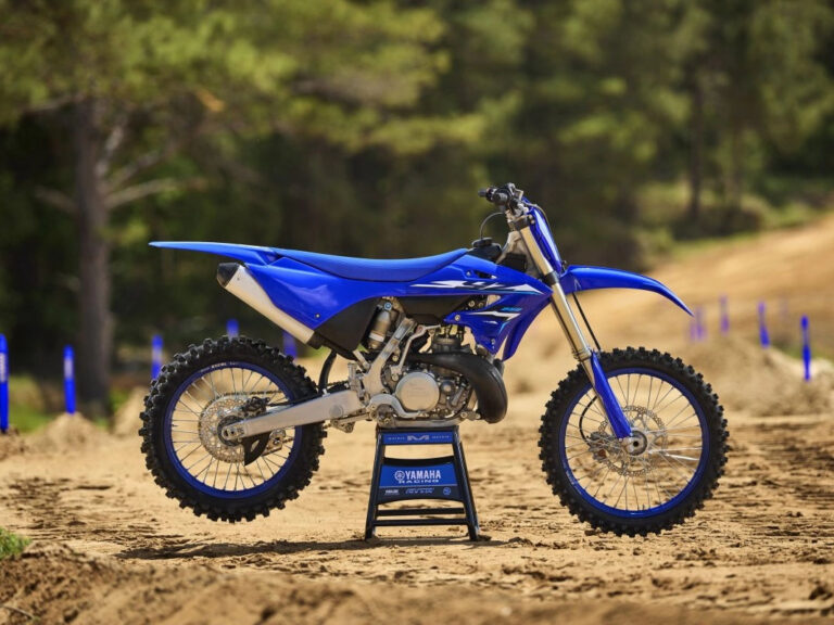 Blue Yamaha dirt bike on a stand, parked on a sandy track with trees in the background.