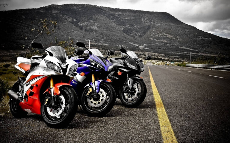 Line of sport motorcycles parked on a sunlit road with mountains in the background